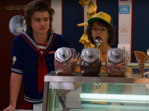 steve looking at dustin eating ice cream off a scoop at scoops ahoy in stranger things