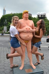 two young ladies pose with a naked trump poster