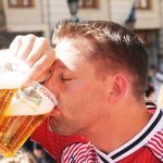 a football fan drinks from one of the two cups of beer he is holding in his right hand
